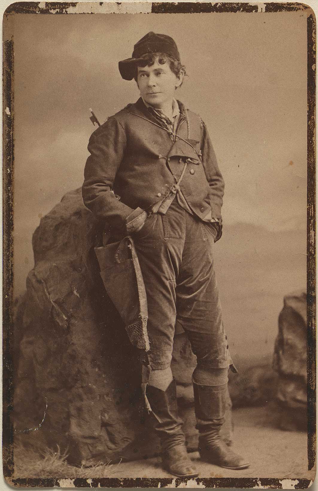 A sepia toned old photograph of a young man leaning against a rock