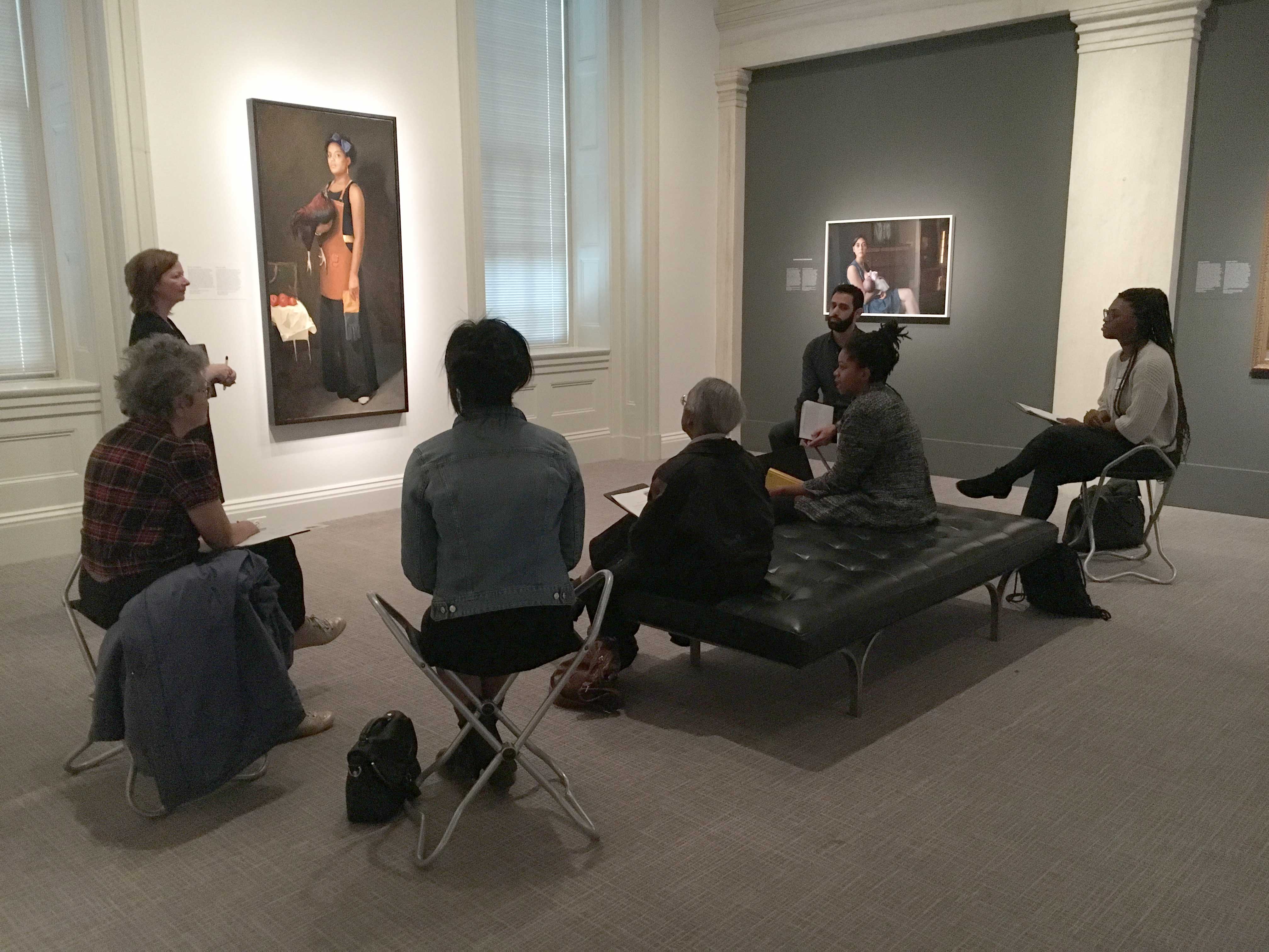 A woman standing in front of a portrait with adults seating in a semi-circle around her