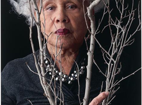 woman with gray hair posing behind a gray branch