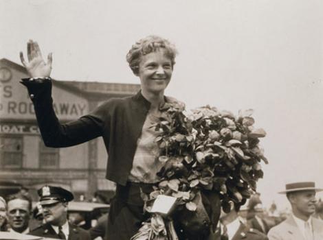 Amelia Earhart waving and holding a bouquet of flowers