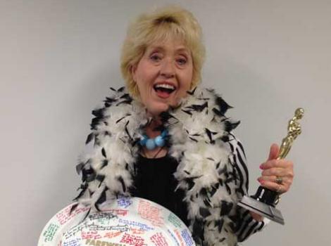 Amy Henderson, wearing feather boa and with replica Oscar in her hand