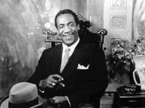 Black and white photo of Bill Cosby, sitting and dressed in a suit