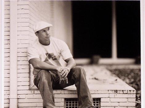 Black and white photo of David Mirra, sitting next to brick building