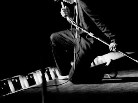 Black and white photo of Elvis oncent, holding microphone and kneeling on stage