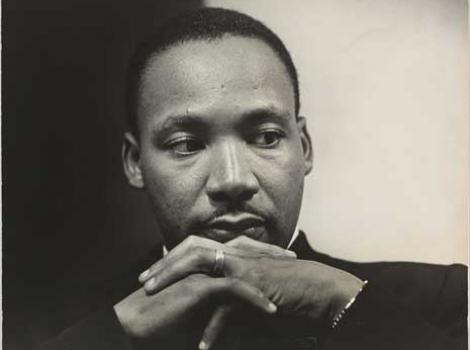 Black and white photograph portrait of Martin Lither King, with hands crossed underneath chin