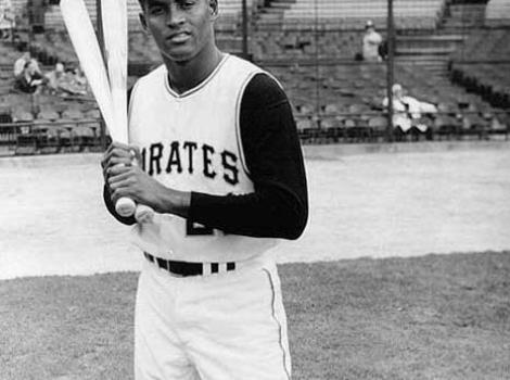 Black and white photo of Roberto Clemente, in Pirates uniform, with two bats on his shoulder