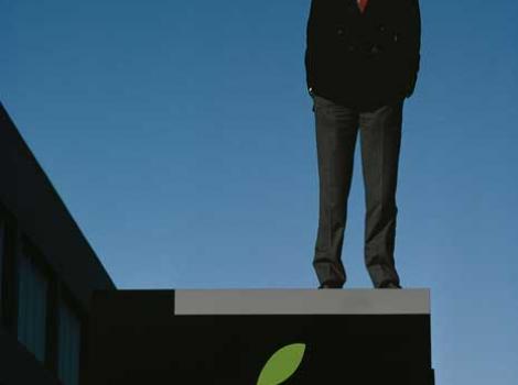 Photograph portrait of Steve Jobs standing on building, above the Apple logo 