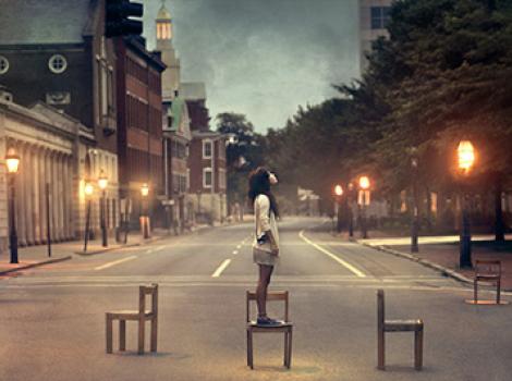 Portrait of young woman in the middle of the street, standing on chair looking upwards