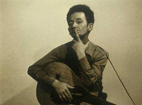 Sepia-toned photograph of Woody Guthrie with guitar