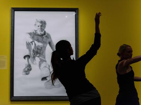 Silhouette of women dancing against a yellow wall with a portrait on it