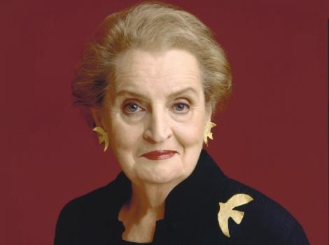 A photograph of a woman staring at the viewer wearing a black suit and a dove pin