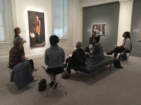 A woman standing in front of a portrait with adults seating in a semi-circle around her