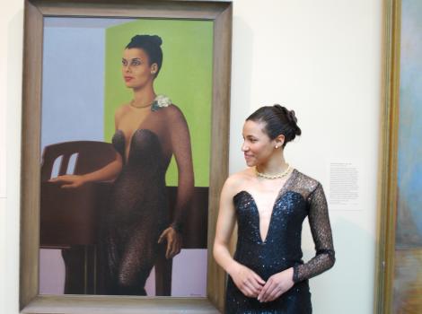 Woman dressed in black dress stands in front of a portrait and looks to the left