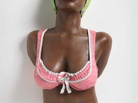Wall-mounted sculpture of the torso and head of a woman in a bathing suit and cap, eyes closed.