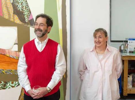 Richard and Fran Morris Rosman, smiling, standing in a room side-by-side, next to a painting