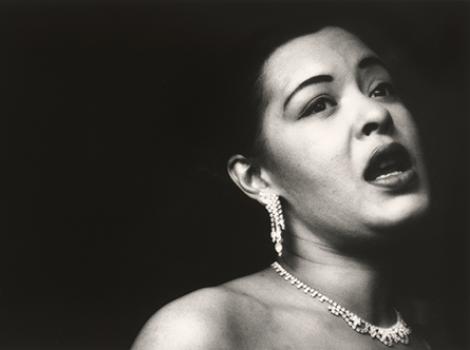 Black and white headshot photo of Billie Holiday, wearing earrings and a necklace.