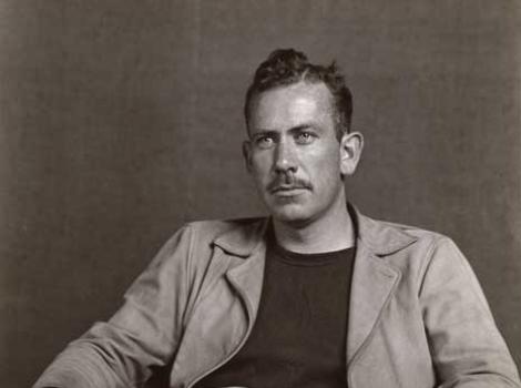 Black and white photo of John Steinbeck seated in an armchair against a neutral background.