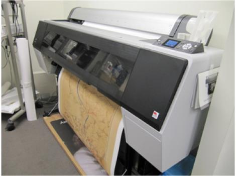 Color photo of a large electronic graphics printer, printing an image on white paper.