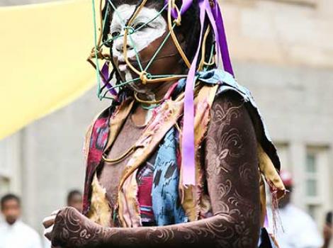 Woman in colorful clothing with wire cage over her face and facial paint