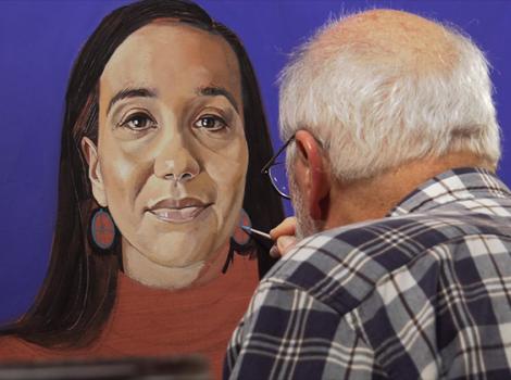 Gray haired man painting a colorful portrait of a woman