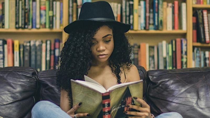Young woman in a black hat reading a book on a leather couch