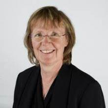 Head shot of a woman with short blonde hair, glasses, and a black shirt.