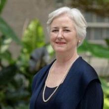 gray haired woman in a blue dress wearing pearls