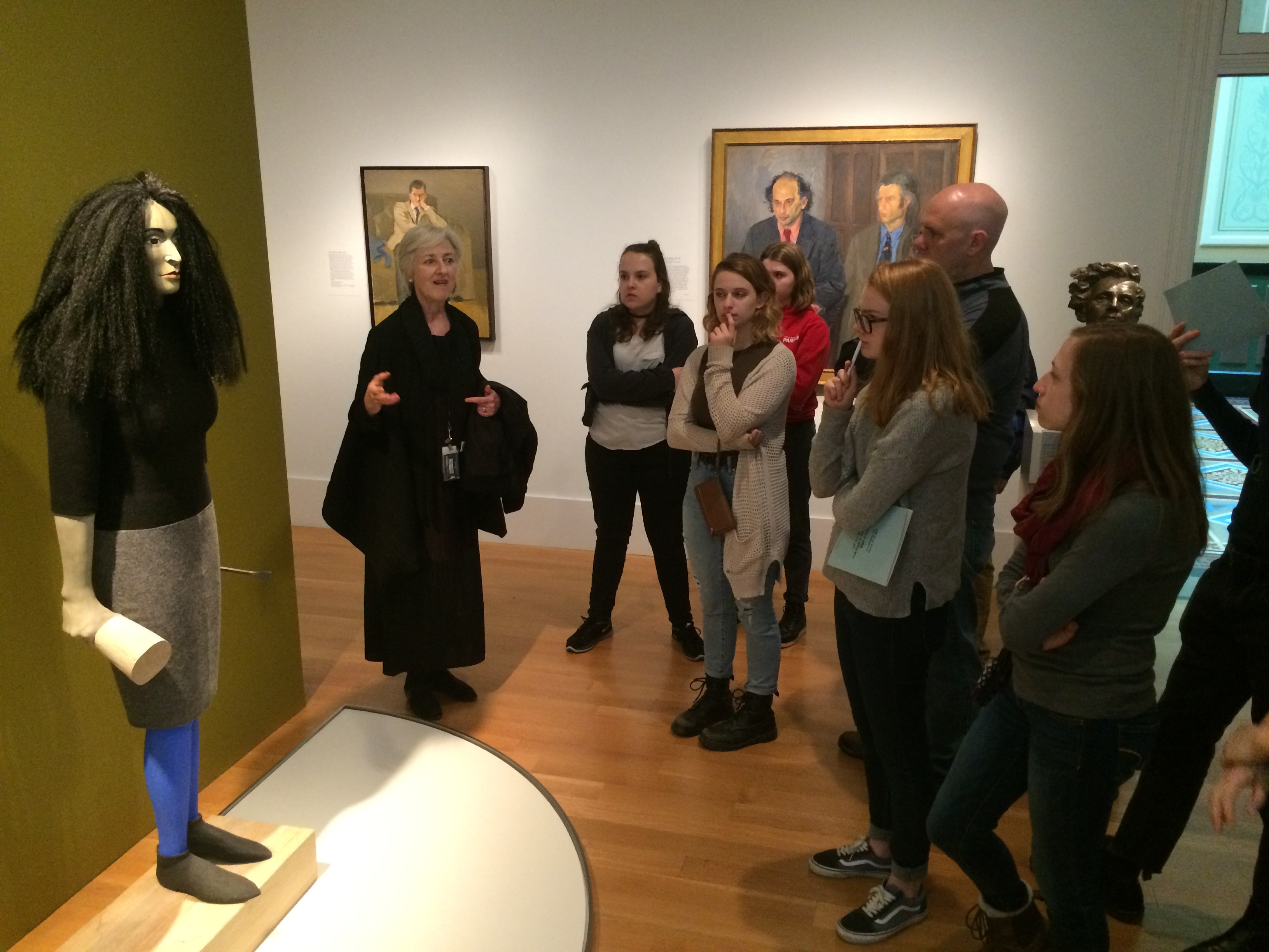 A group of young people gathered around a sculpture being spoken to a woman