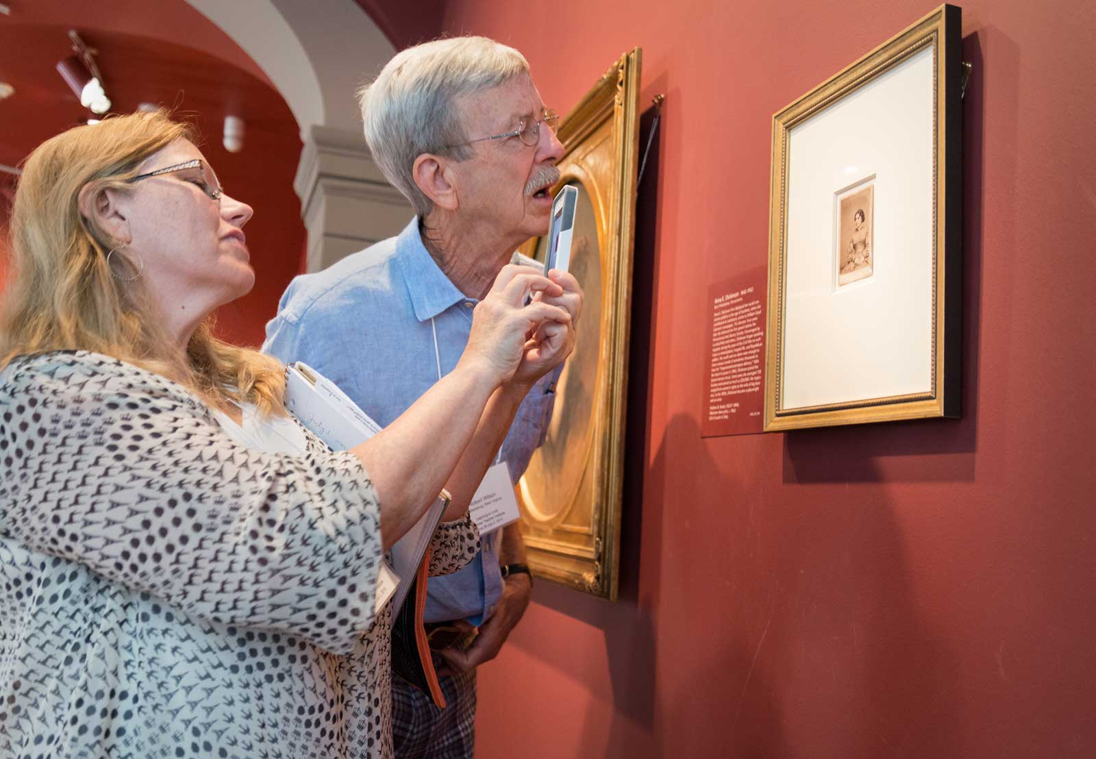 Two people taking pictures of a portrait on a wall