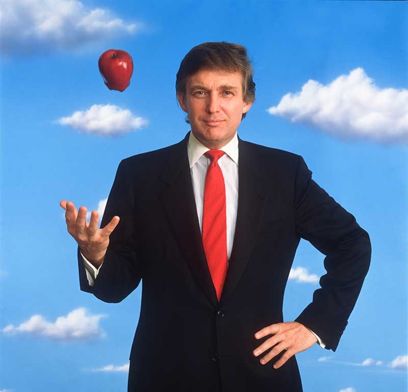 Photograph portrait of Donald Trump in a suit and tossing an apple in the air.  The background is blue sky with clouds.