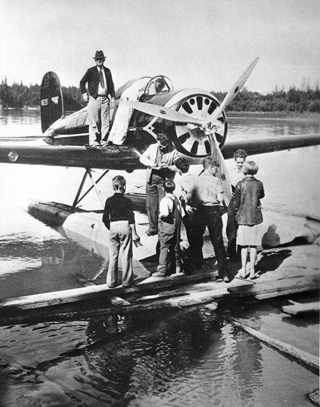 man and children standing on the pontoons of a plane while one man signs autographs